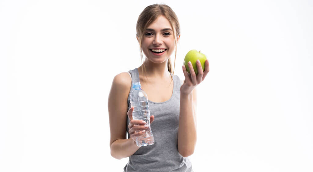 Junge Frau hält lächelnd Apfel und Wasserflasche in den Händen