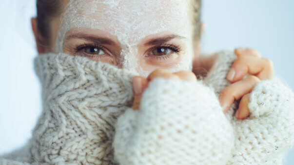 Frau im Winterpulli mit Gesichtsmaske symbolisiert Hautpflege im Winter